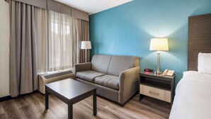 Ein Hotelzimmer mit einer Couch, einem kleinen Tisch, einem Nachttisch mit Lampe, einem Telefon und einem Bett.