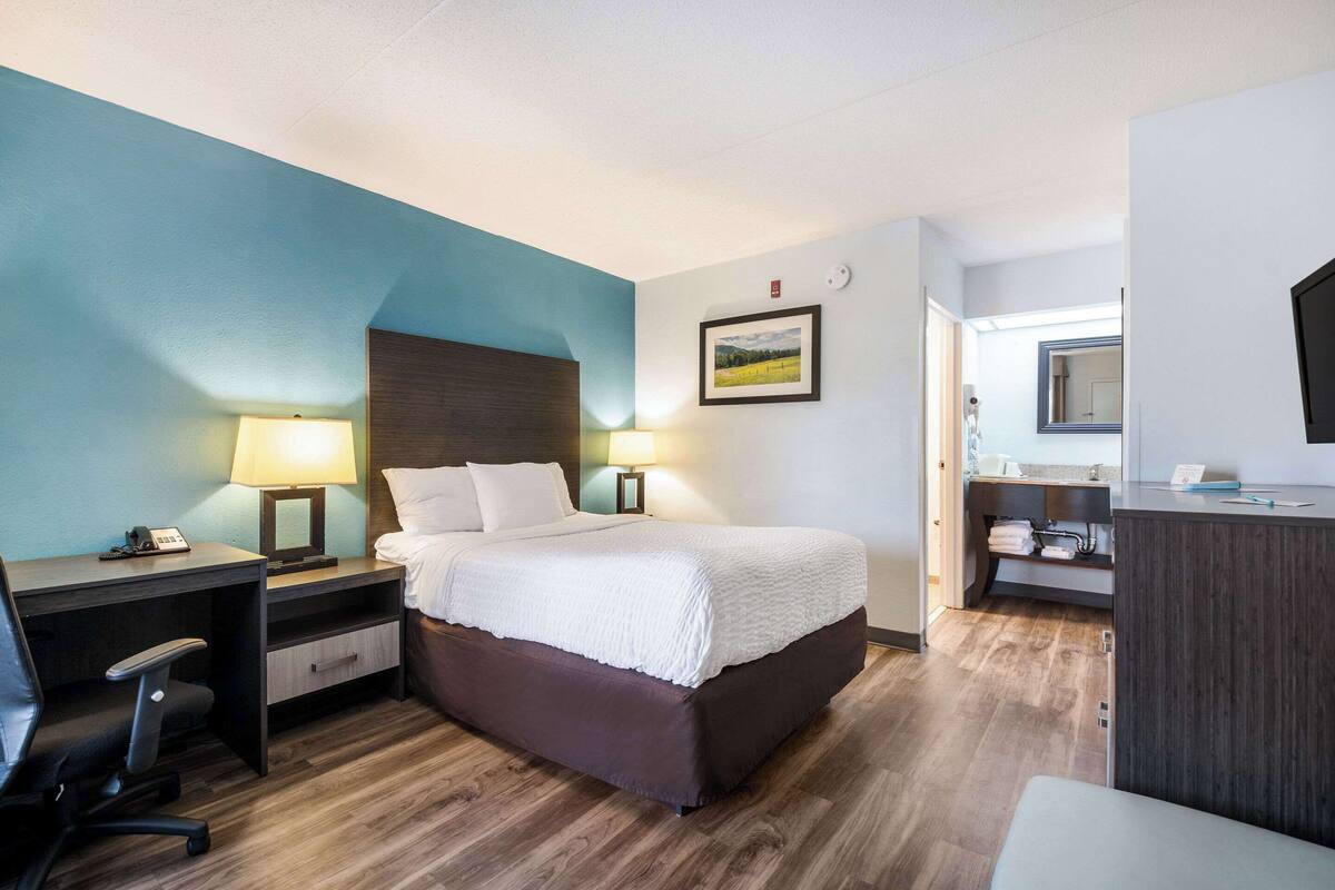 A hotel room with a bed, desk, chair, and a bathroom area.