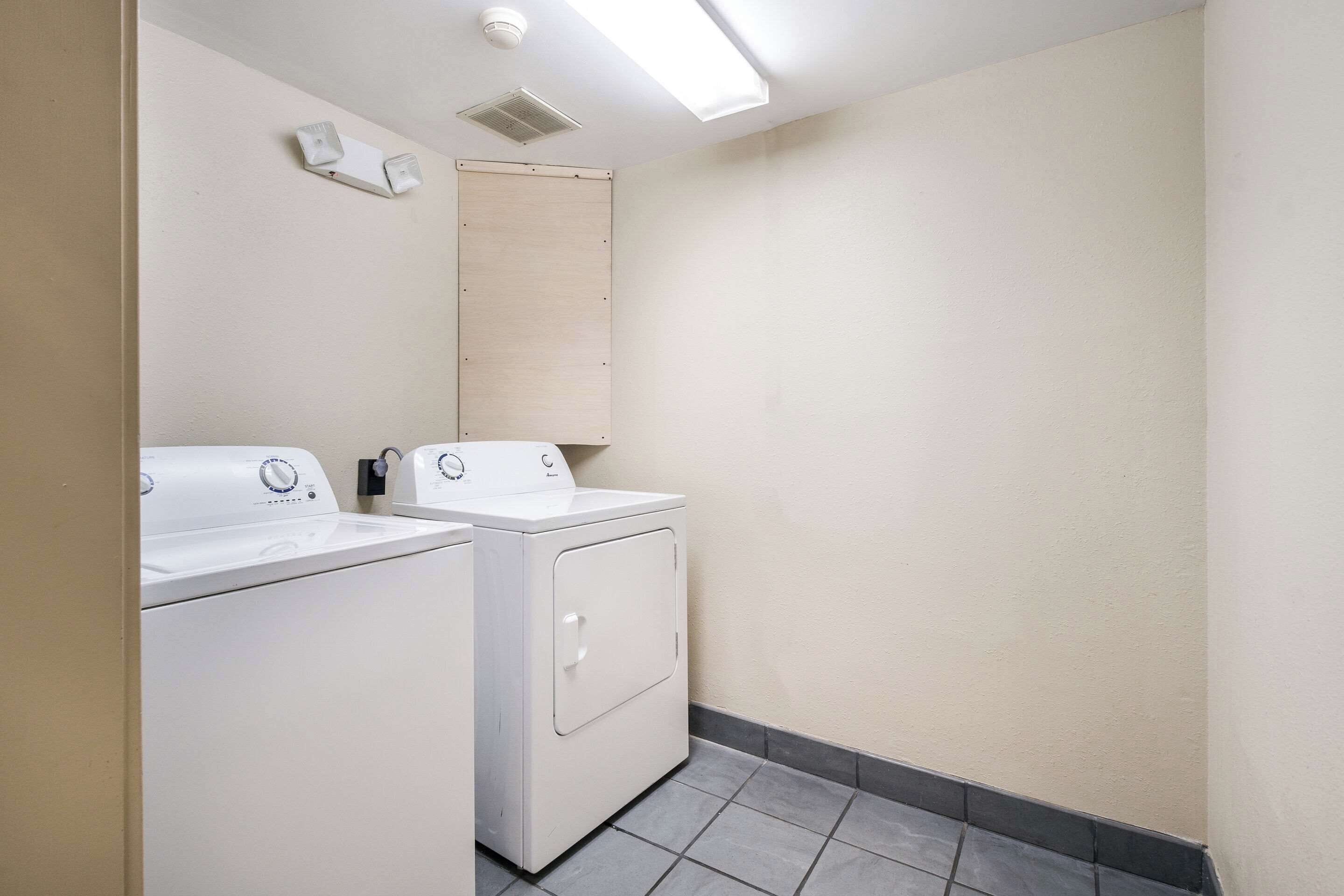 Un cuarto de lavado con dos lavadoras y secadoras blancas, una lámpara y una puerta de madera.
