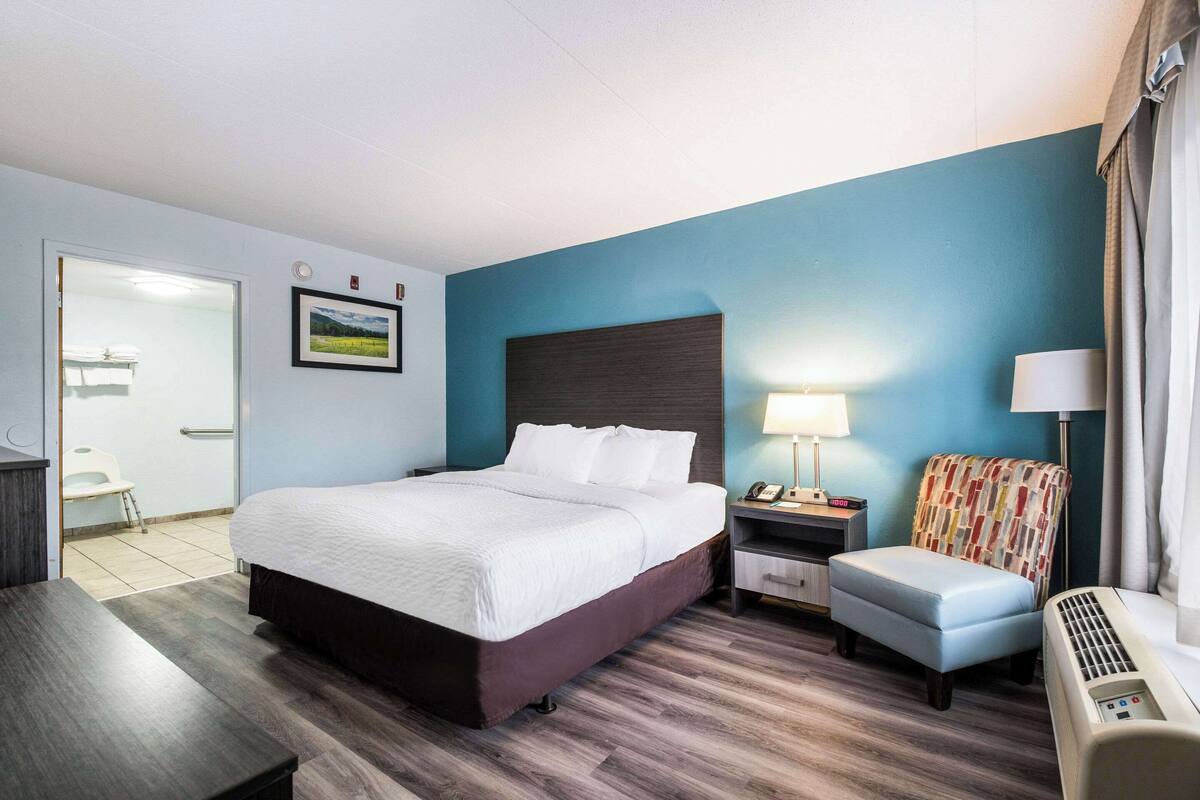 A hotel room with a large bed, bedside table, chair, and a heater.