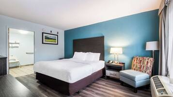 A hotel room with a large bed, bedside table, chair, and a heater.