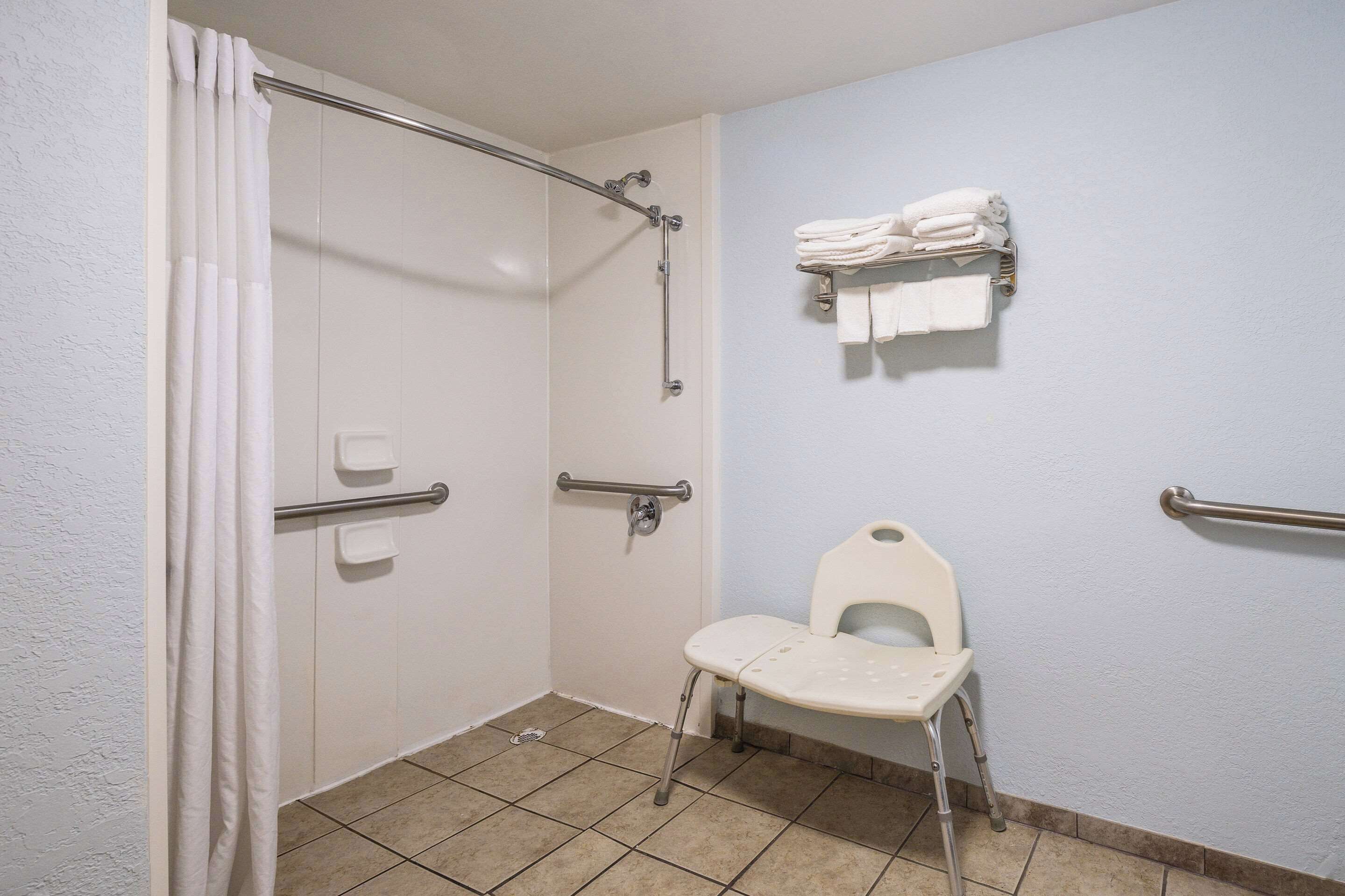 A bathroom with a shower, a toilet, and a wheelchair-accessible chair.