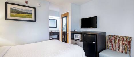 A hotel room with a bed, a desk with a microwave, a television, and a small seating area.