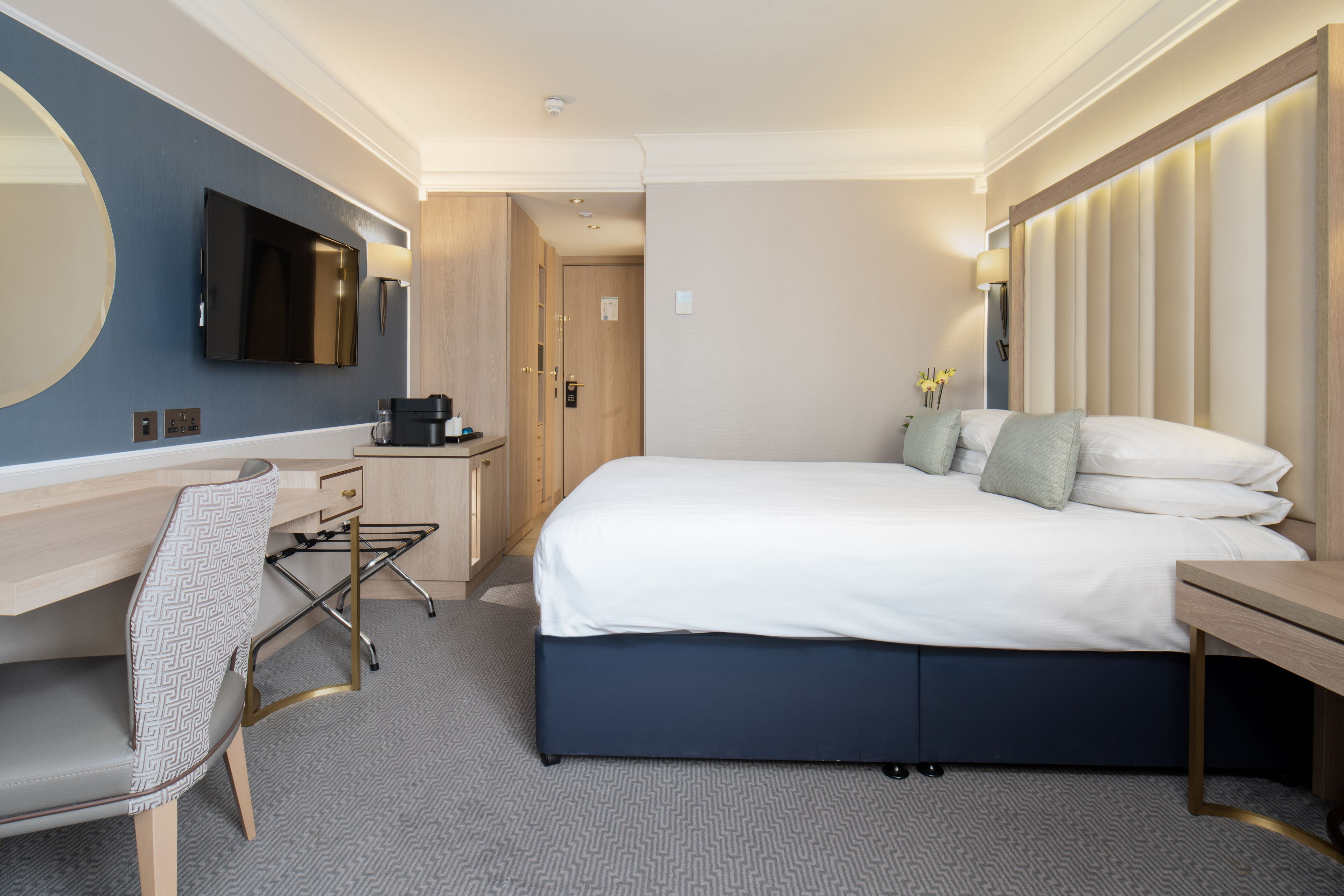 A hotel room with a bed, desk, chair, TV, and a large mirror.