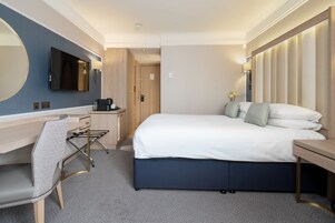 Ein Hotelzimmer mit Bett, Schreibtisch, Stuhl, Fernseher und einem großen Spiegel.