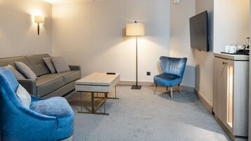 A modern living room with a sofa, two armchairs, a coffee table, a floor lamp, and a TV mounted on the wall.