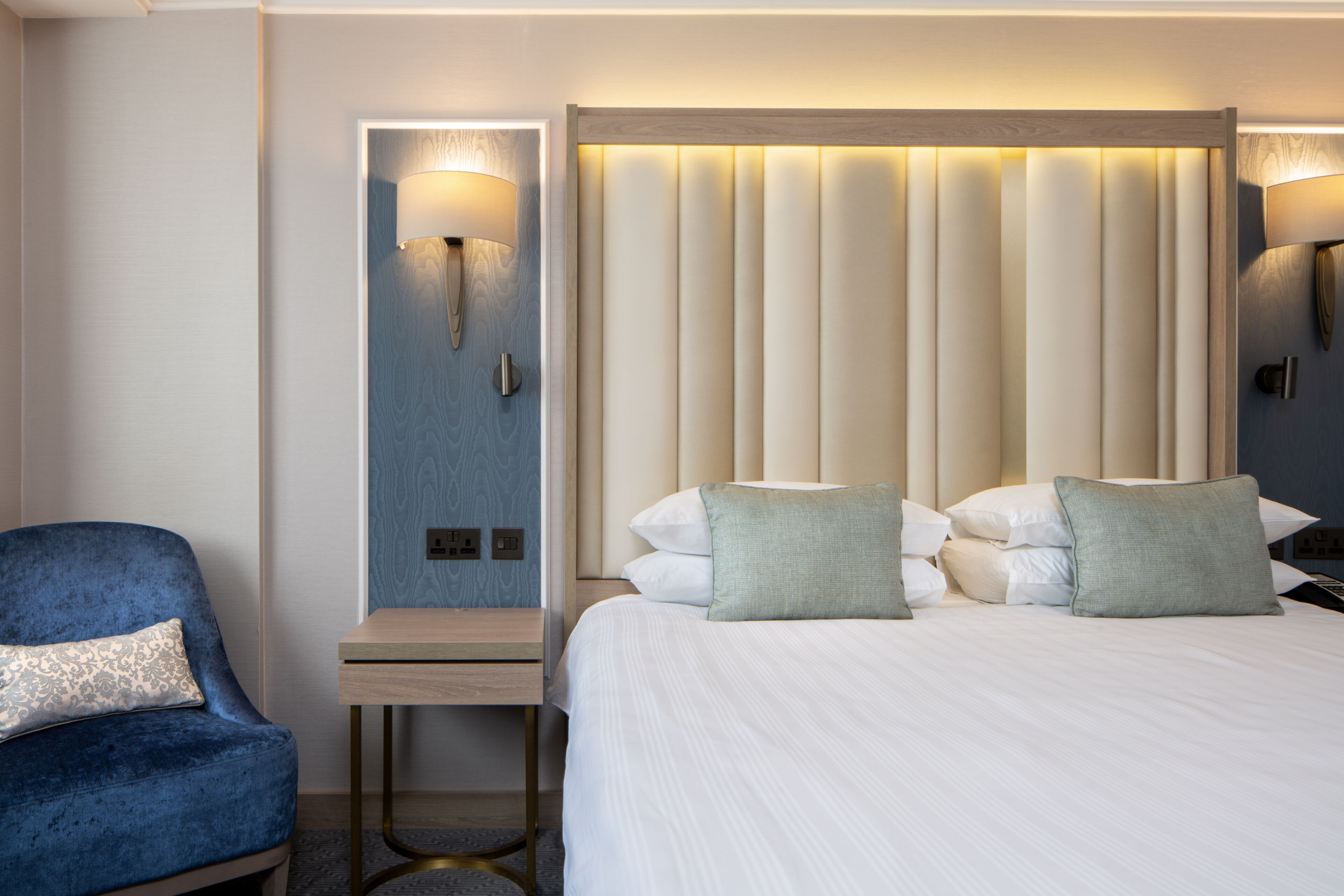 Quarto de hotel com uma cama, uma escrivaninha, uma cadeira e duas luminárias de parede.
