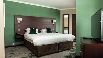 A hotel room with a large bed, two bedside tables with lamps, a TV on a dresser, and a green wall.