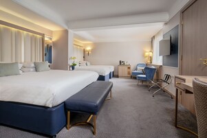 A hotel room with two beds, a desk, a chair, a TV, and a small table.