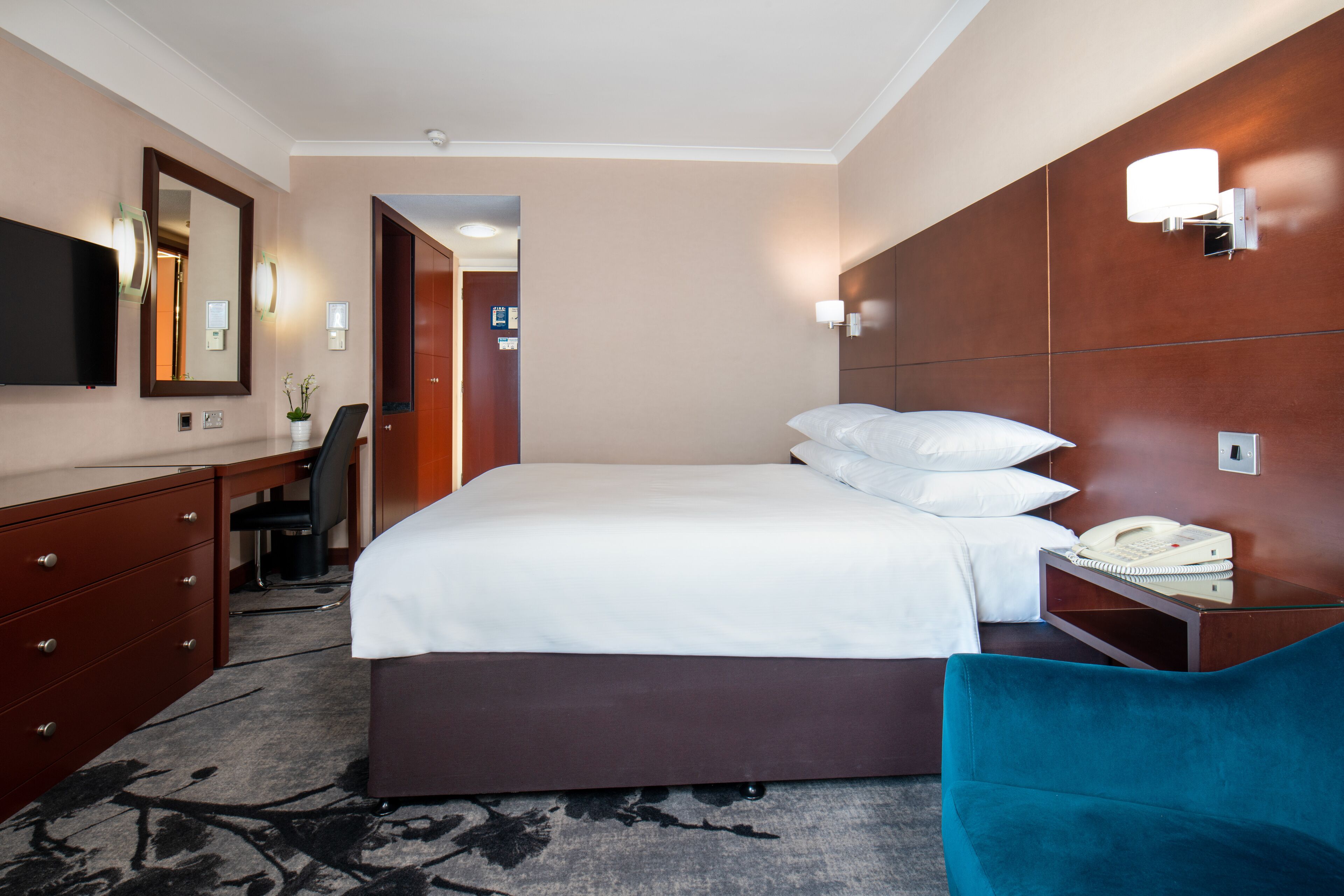 A hotel room with a large bed, a desk with a chair, a television, and a telephone on a side table.