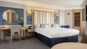 A hotel room with a large bed, a desk with a chair, a mirror, and a wardrobe.