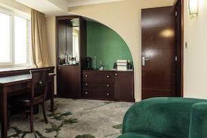 A room with a desk, chair, and a green couch. There is a wardrobe with a mirror and a green wall.