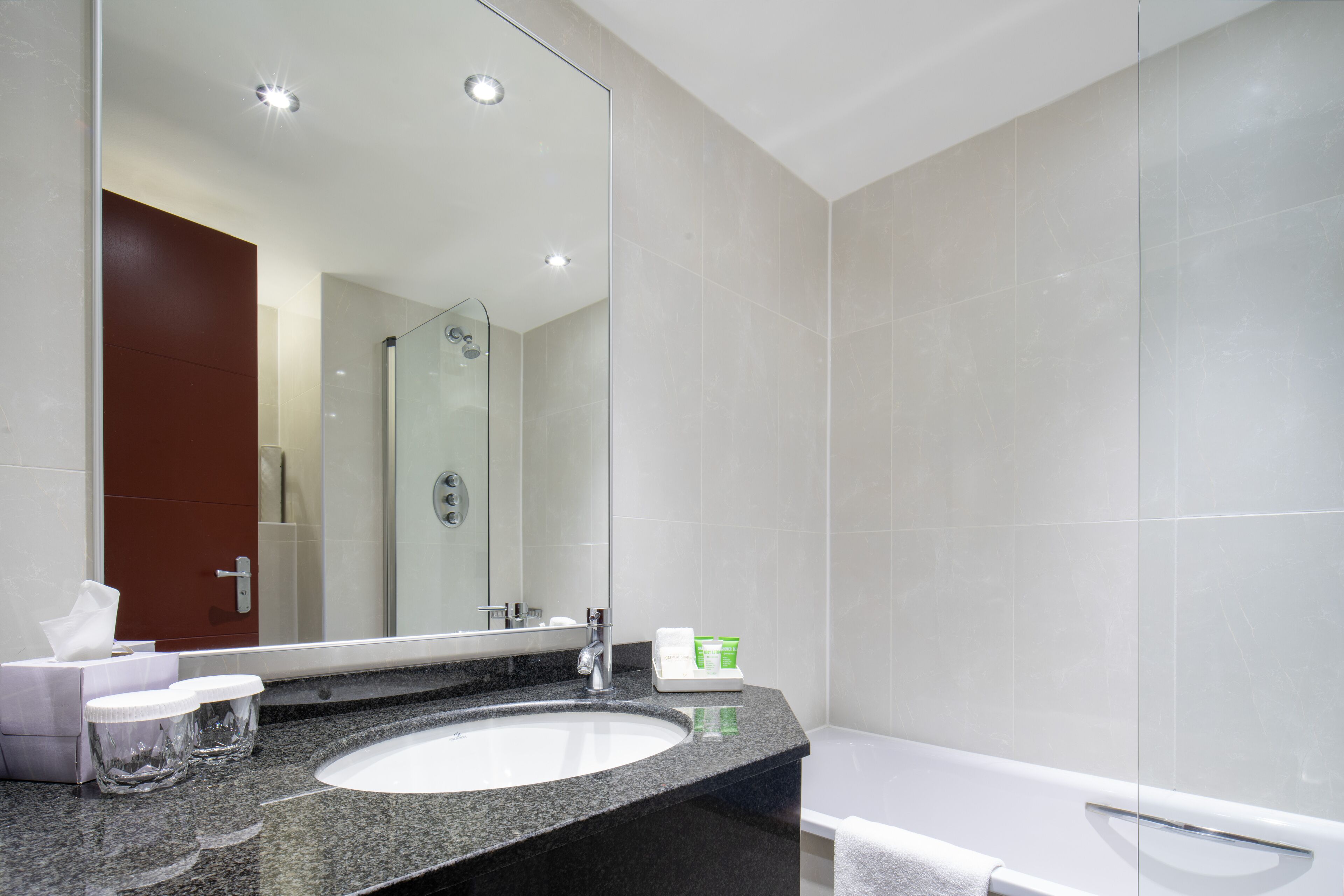 Ein modernes Badezimmer mit einem großen Spiegel, einem Granitwaschbecken, einer weißen Badewanne und einer Duschkabine aus Glas.