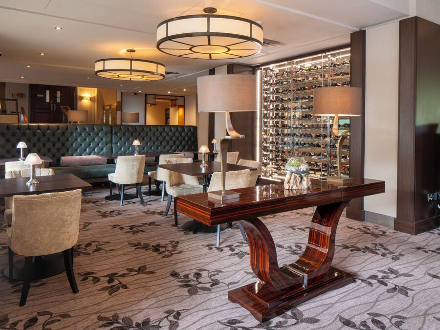 Un hall d’hôtel comprenant un espace salon, un présentoir à bouteilles de vin et un comptoir de réception.