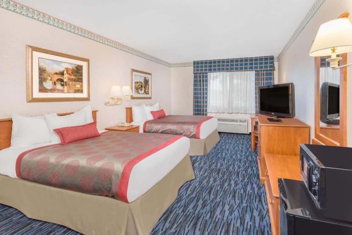 A hotel room with two beds, a television, a desk with a computer, and a window with curtains.