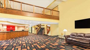 A hotel lobby with a reception desk, a staircase, a leather sofa, and a patterned carpet. - Ramada by Wyndham Kent Seattle Area (Kent)