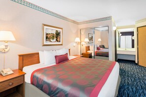A hotel room with a large bed, bedside lamps, a nightstand, a telephone, a framed picture on the wall, and a mirror. - Ramada by Wyndham Kent Seattle Area (Kent)