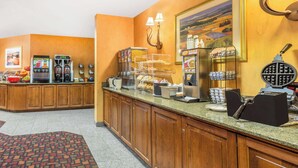 A hotel lobby with a coffee station, a buffet area, and a painting on the wall. - Ramada by Wyndham Kent Seattle Area (Kent)