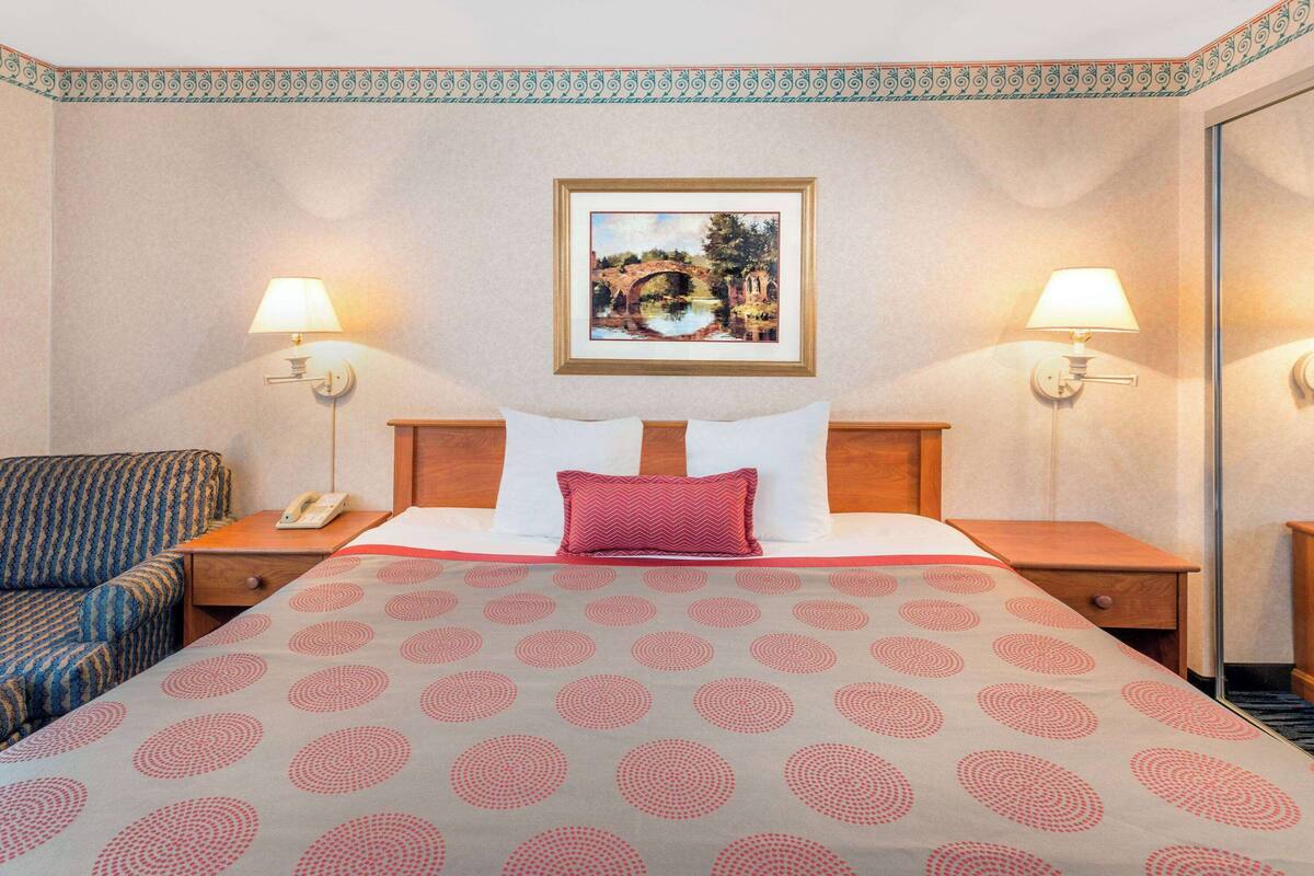 A hotel room with a bed, two bedside lamps, a telephone, a patterned bedspread, and a framed picture on the wall.