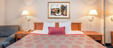Habitación de hotel con cama, dos lámparas de noche, un teléfono, una colcha estampada y un cuadro en la pared.