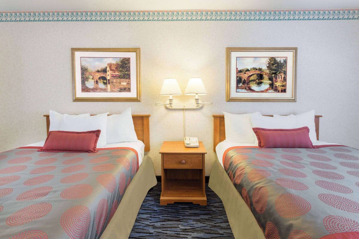 A hotel room with two beds, each with a patterned bedspread, a nightstand with a lamp, and framed pictures on the wall.