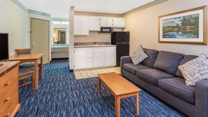 A compact hotel room with a kitchenette, a sofa, a wooden table, and a television. - Ramada by Wyndham Kent Seattle Area (Kent)