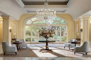 A grand room with a large chandelier, a round table with a floral centerpiece, and two armchairs. - Langham Huntington, Pasadena, Los Angeles (Pasadena)