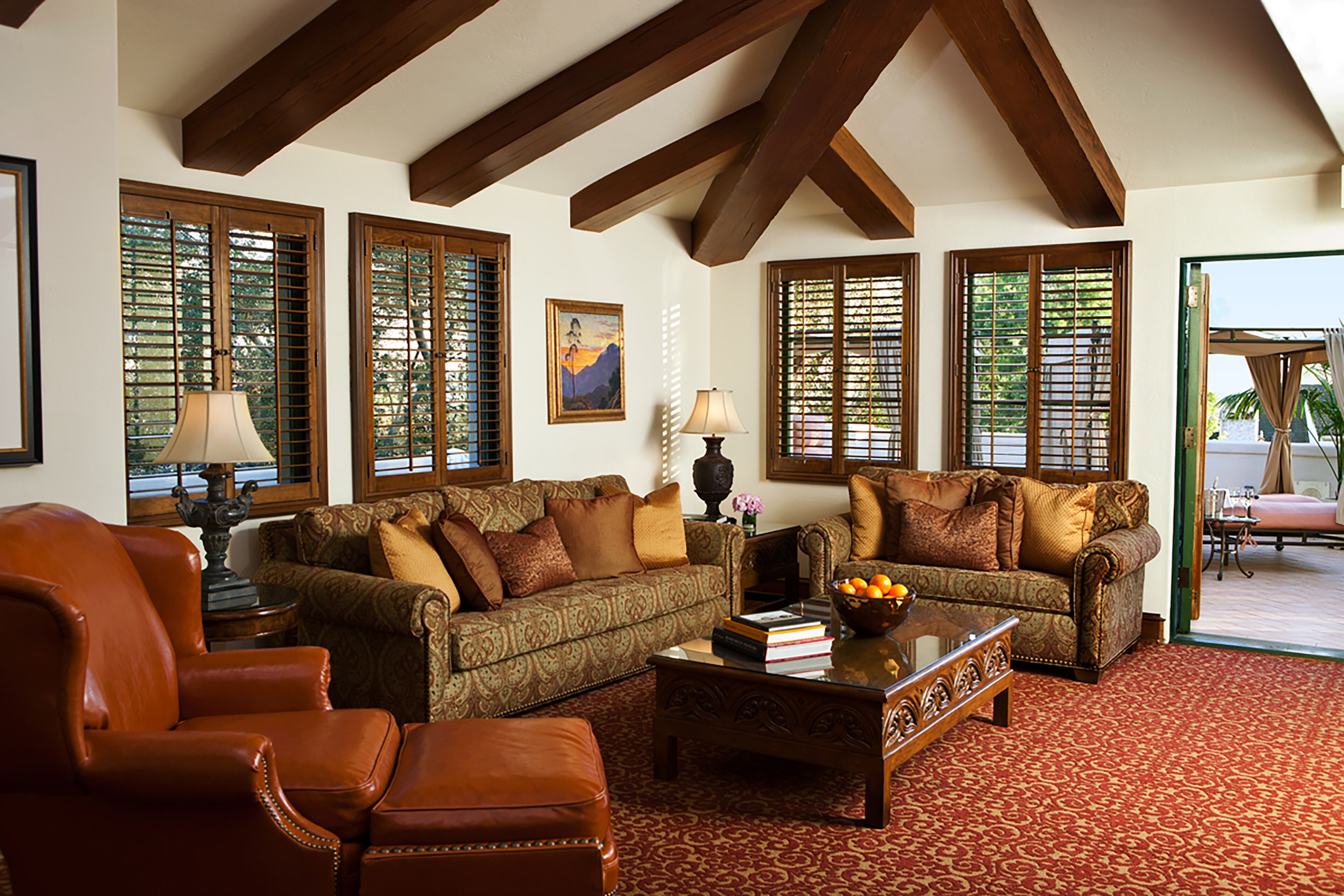 A cozy living room with a brown leather sofa, a matching armchair, and a wooden coffee table with books and a fruit bowl.