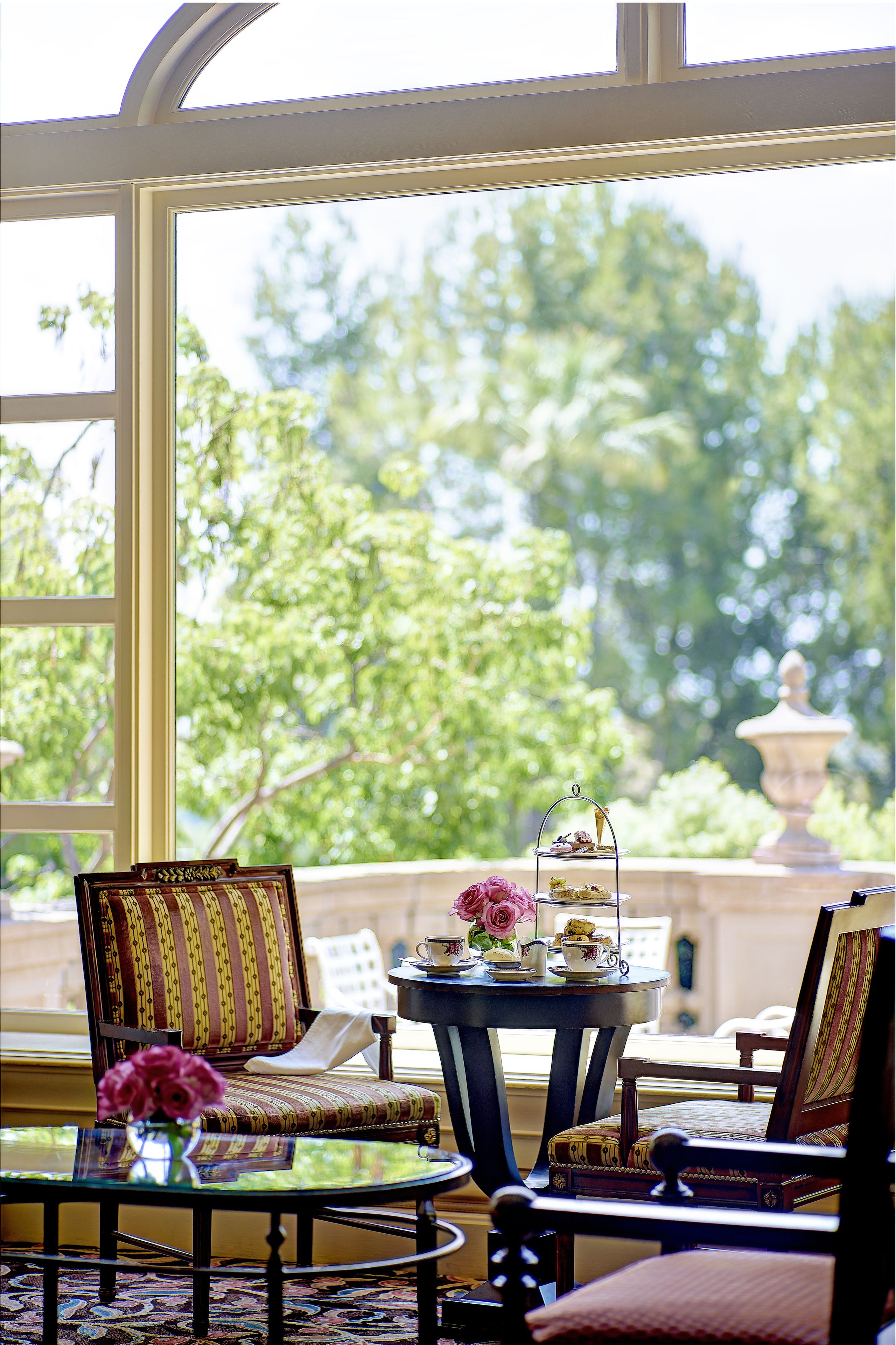A room with a large window, a table with a vase of flowers, and a chair with a striped cushion.