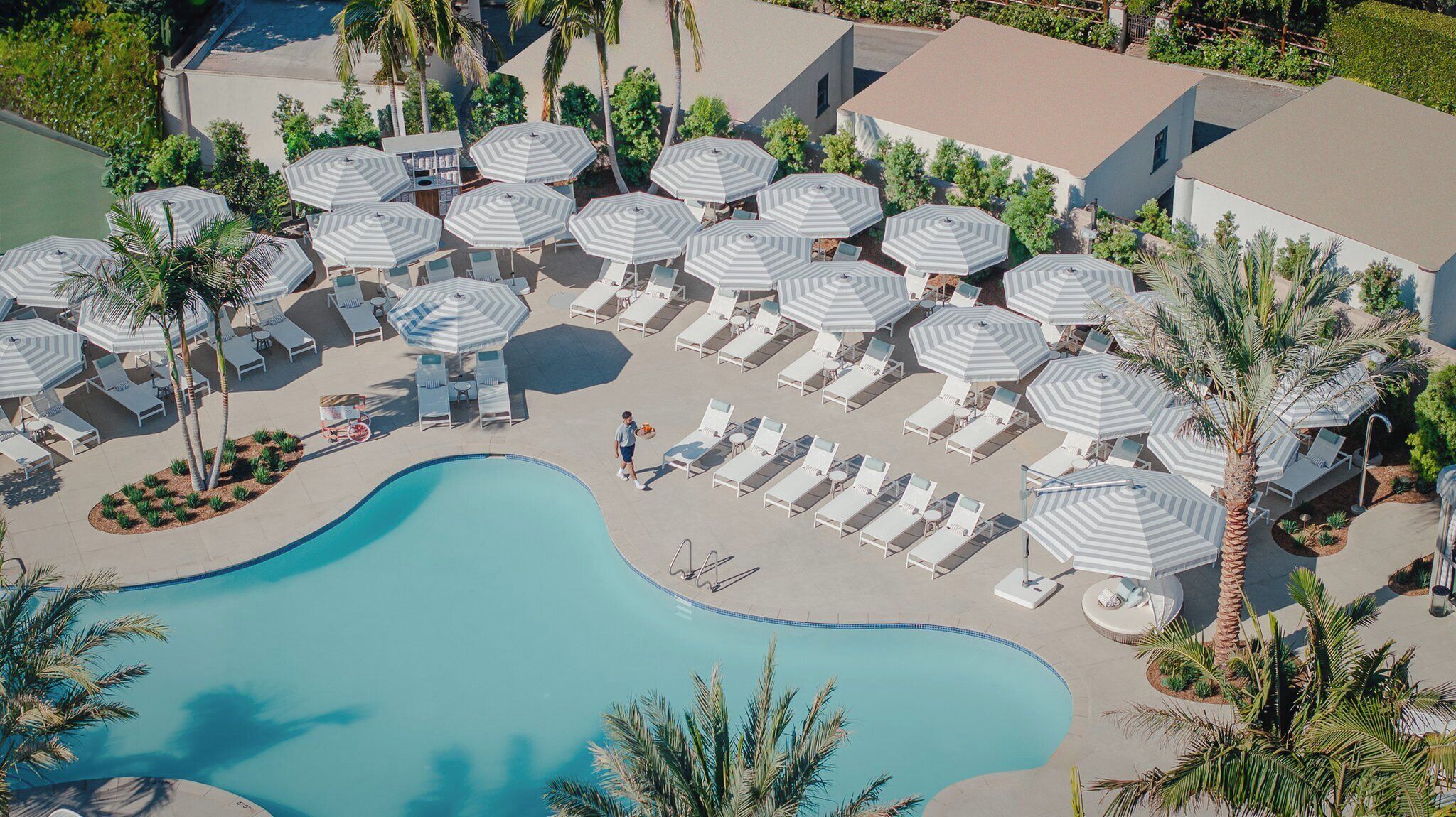An aerial view of a resort with a swimming pool, sun loungers, and striped umbrellas.