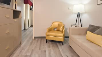 Une pièce avec un canapé beige, un petit fauteuil, une commode en bois et un lampadaire.