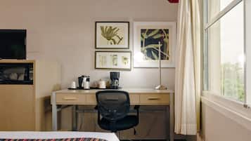Ein Hotelzimmer mit einem Bett, einem Schreibtisch mit Stuhl, einem Fernseher, einer Kaffeemaschine und gerahmten Bildern an der Wand.