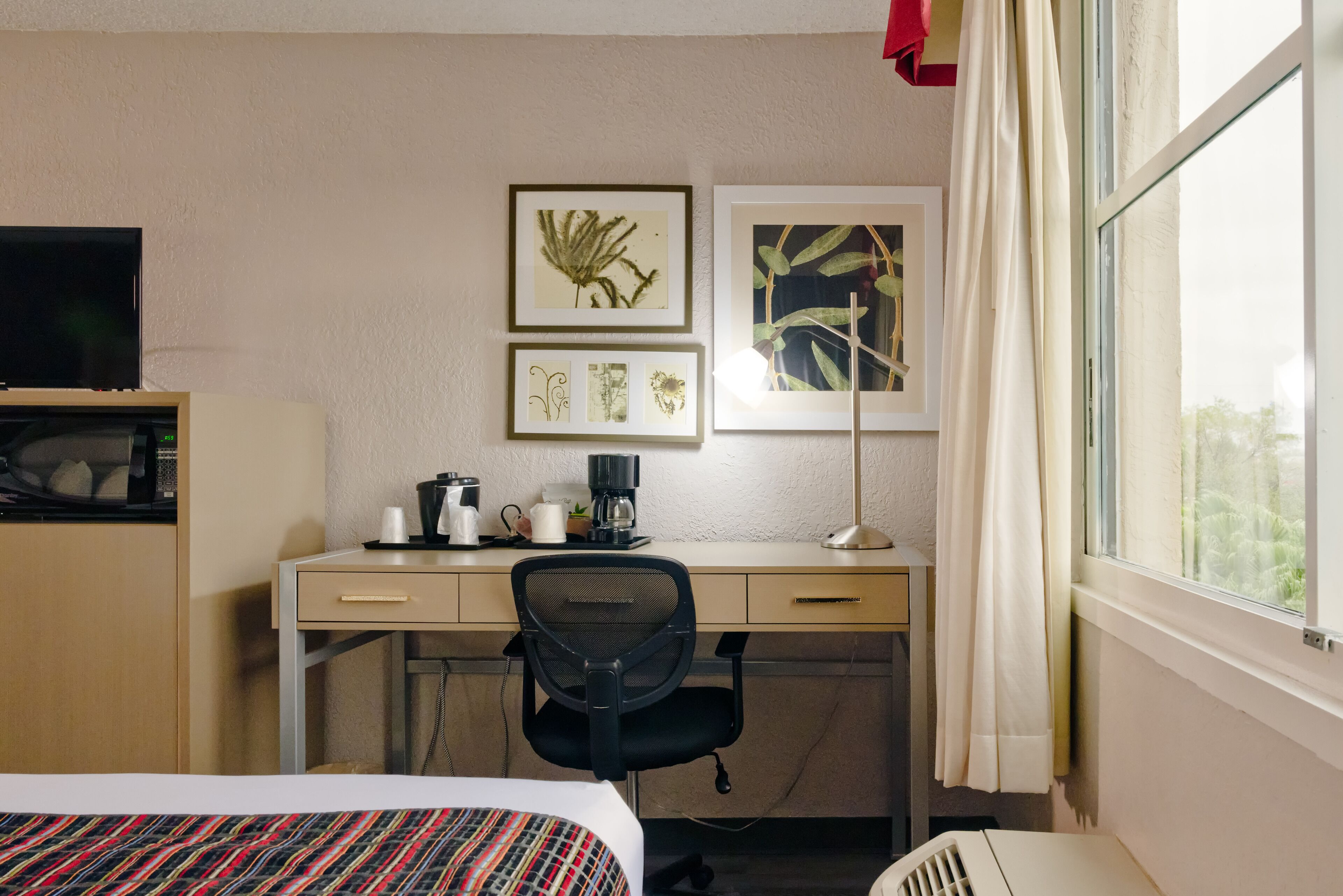 Une chambre d’hôtel avec un lit, un bureau et une chaise, une télévision, une machine à café et des tableaux accrochés au mur.