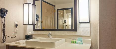 A hotel bathroom with a large mirror, a sink, and a hairdryer on the wall.