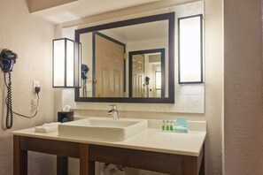 A hotel bathroom with a large mirror, a sink, and a hairdryer on the wall.