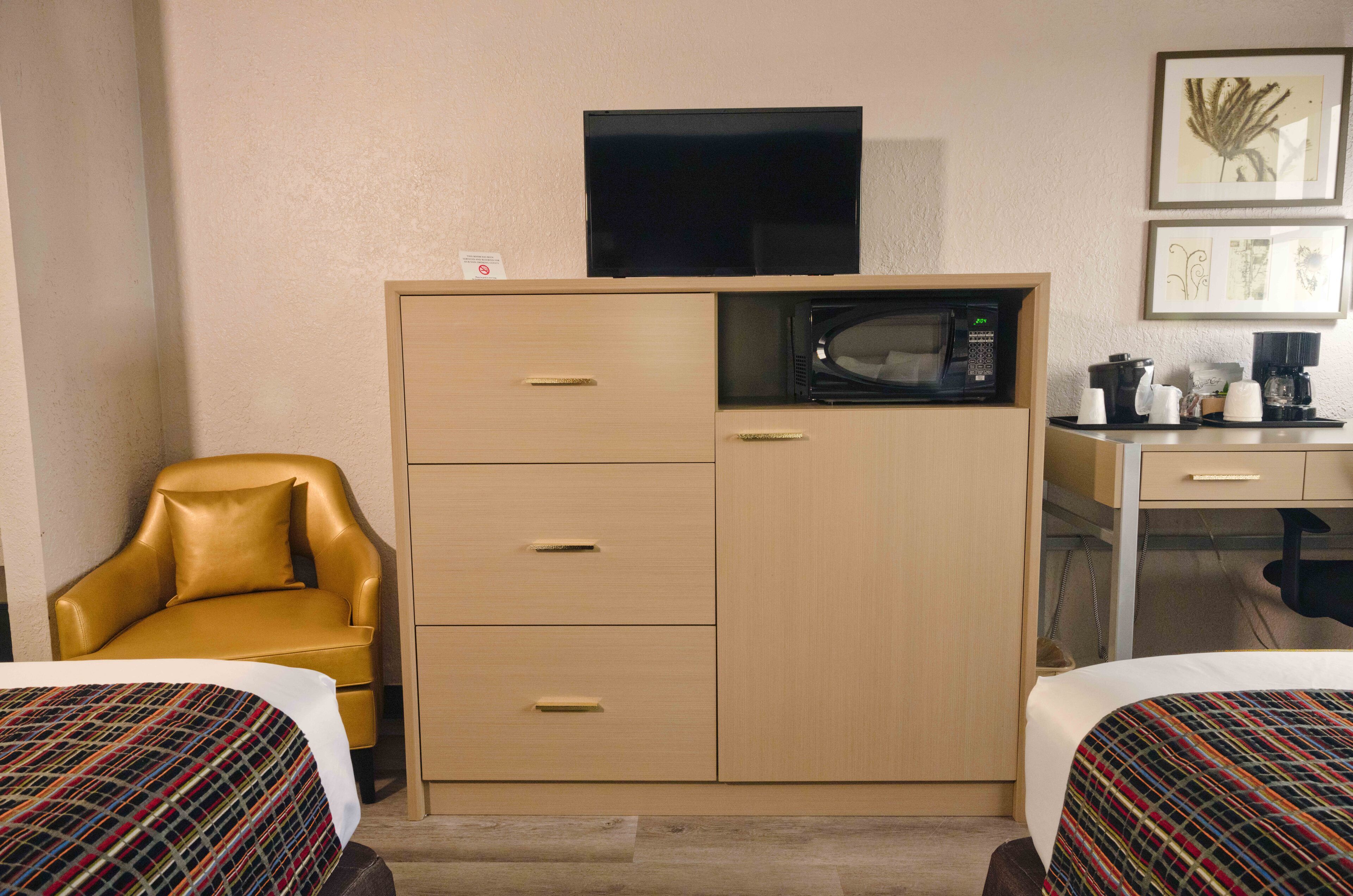 Habitación de hotel con cama, sofá, escritorio con microondas y televisor sobre un mueble.