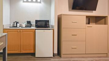 A compact kitchenette with a microwave, coffee maker, and a small refrigerator. There is a wooden cabinet with drawers and a flat-screen TV mounted on the wall.