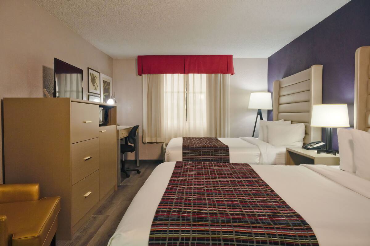 A hotel room with two beds, a desk, a chair, a dresser, and a window with curtains.