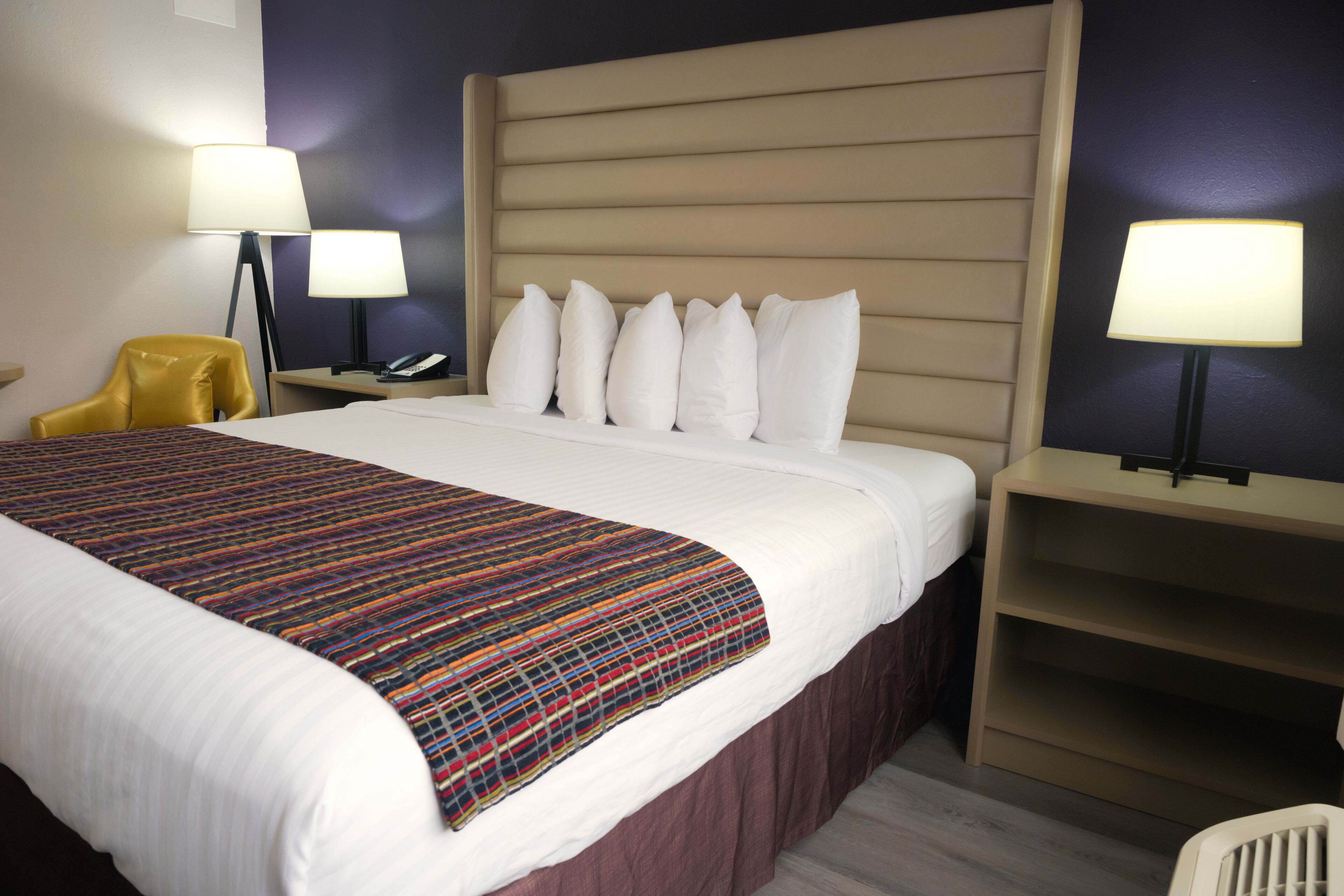 A hotel room with a large bed, a headboard, two bedside tables with lamps, a chair, and a desk.