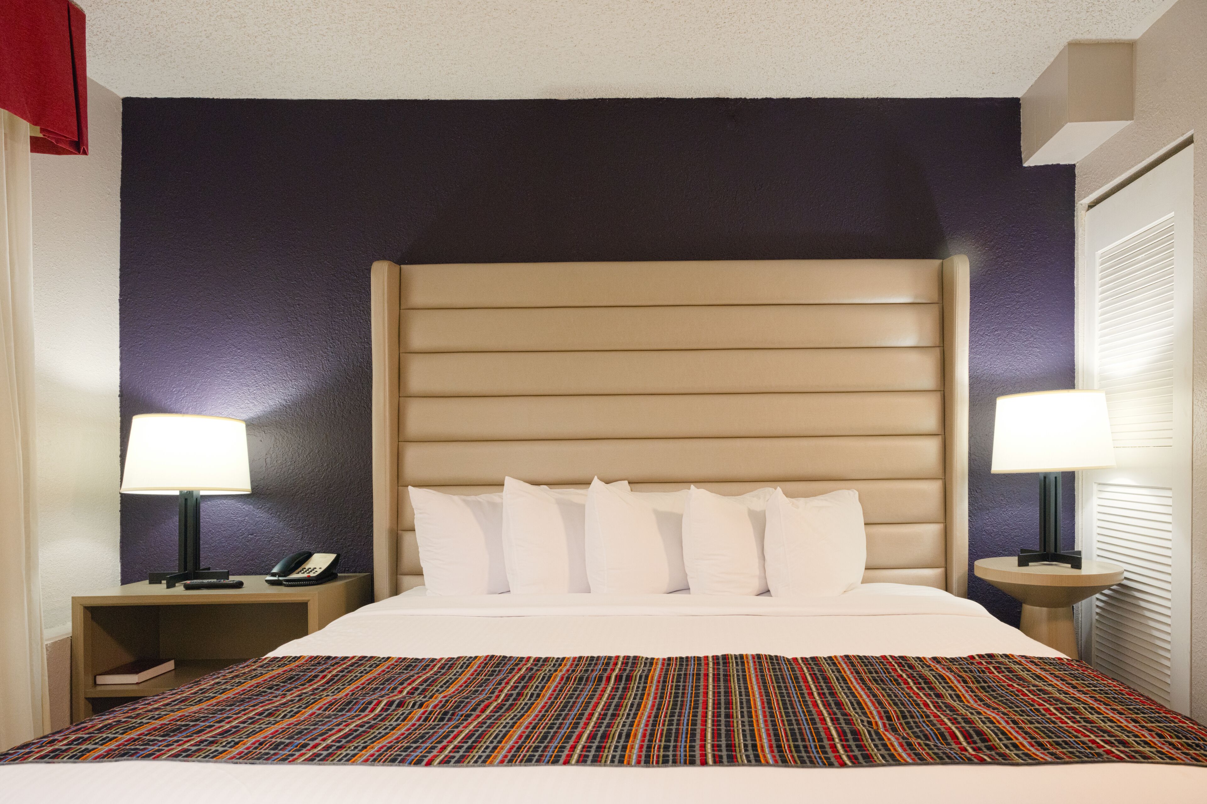 A hotel room with a large bed, two bedside tables, a telephone, and a lamp on each side.