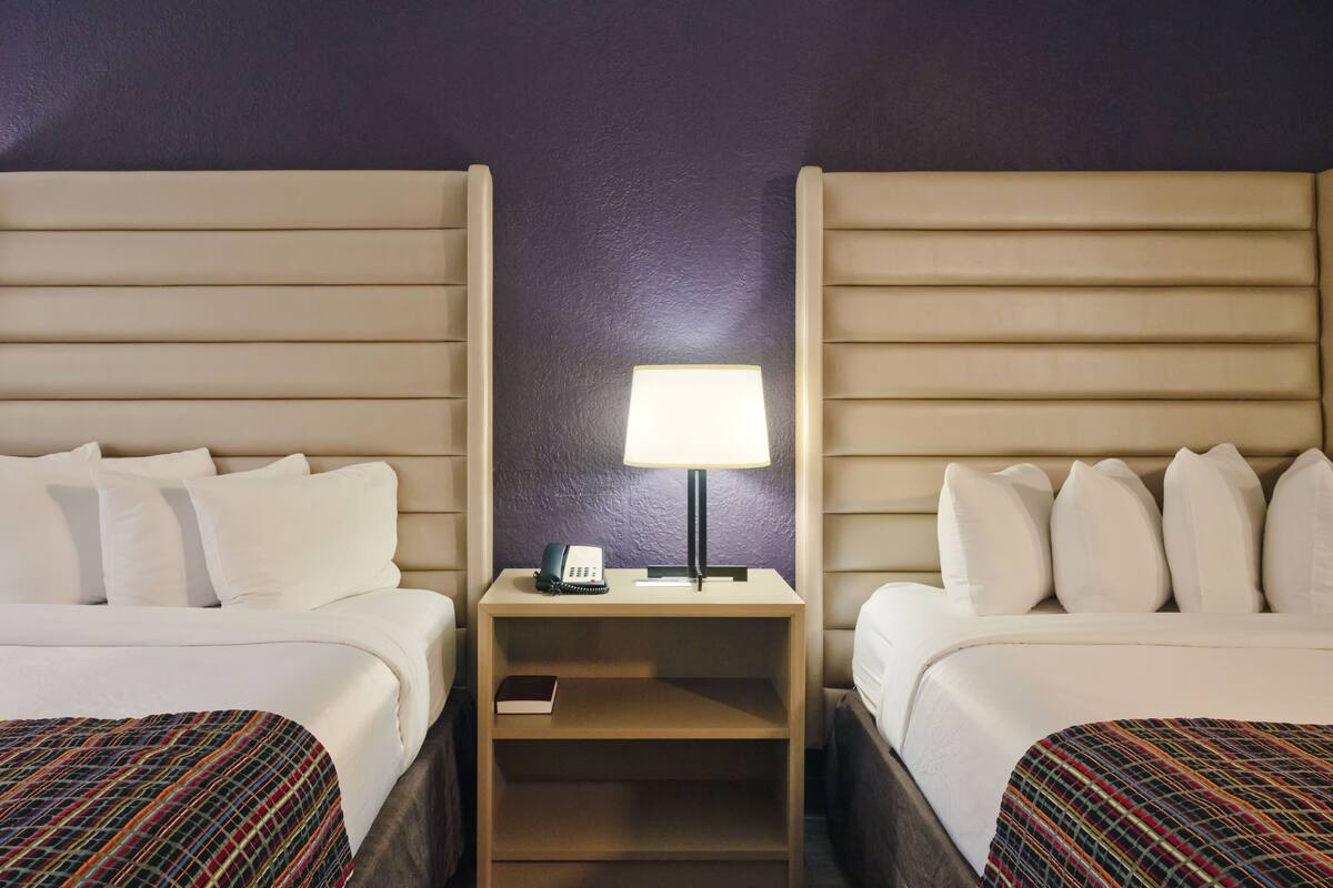 A hotel room with two beds, a nightstand with a lamp, a phone, and a book.