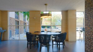 Un vaste espace dédié à la salle à manger, avec une grande table et des chaises, un luminaire suspendu et de grandes fenêtres offrant une vue sur l’extérieur.