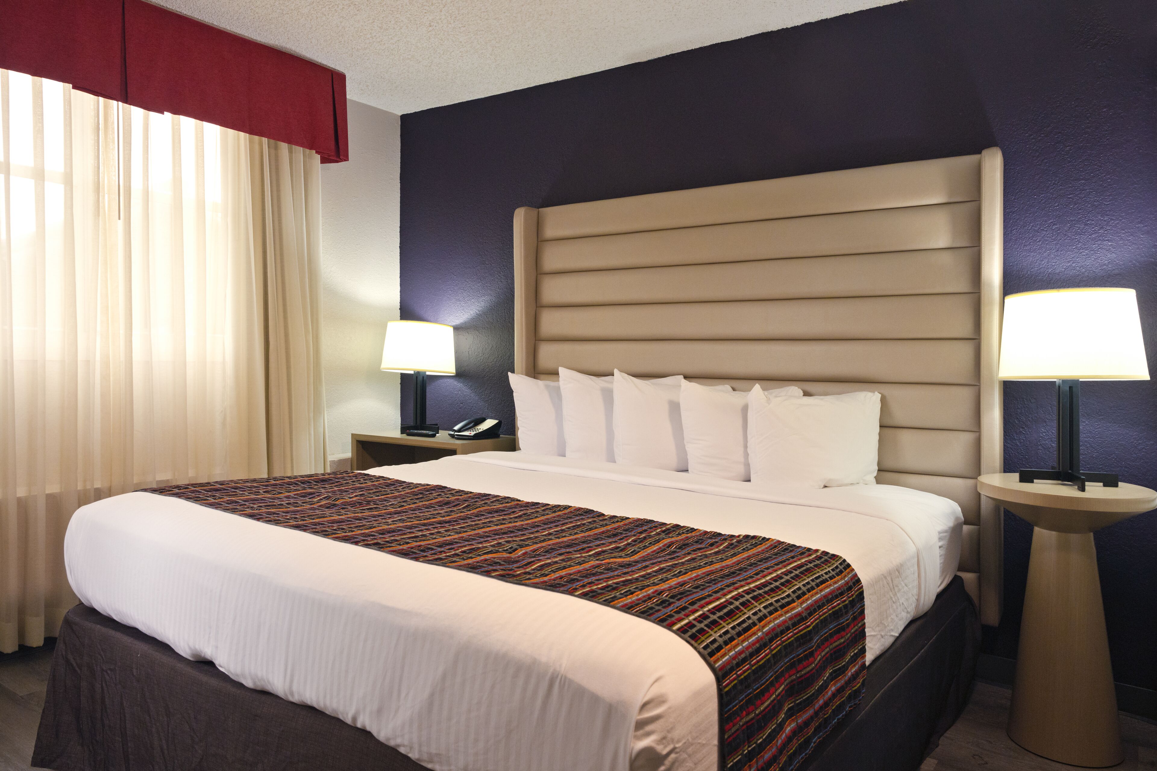 A hotel room with a large bed, two bedside tables with lamps, a red curtain, and a dark blue accent wall.