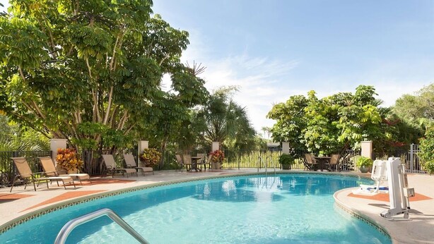 Une piscine entourée d’arbres, avec des chaises longues et des tables.