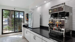 Una cocina moderna con cafetera, refrigerador y ventana con vista a árboles.