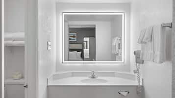 A modern bathroom with a white sink, a mirror with built-in lighting, a hairdryer, and a towel rack.