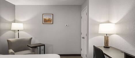 A hotel room with a bed, a desk, a chair, and two lamps.
