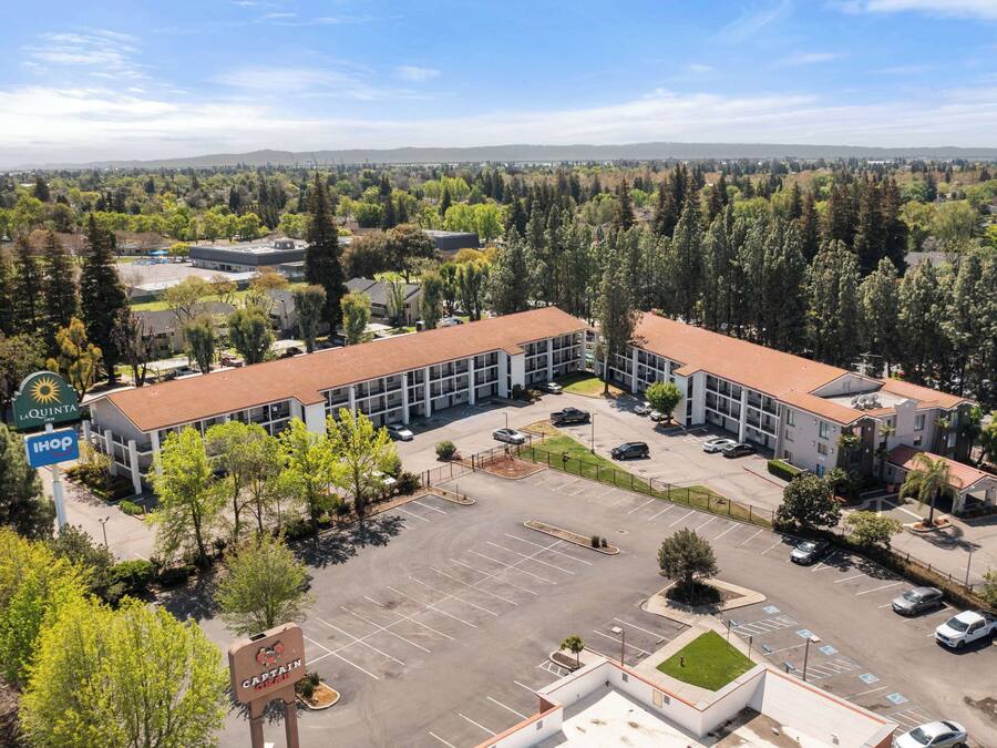 A multi-story hotel with a parking lot and a view of surrounding greenery and distant hills.