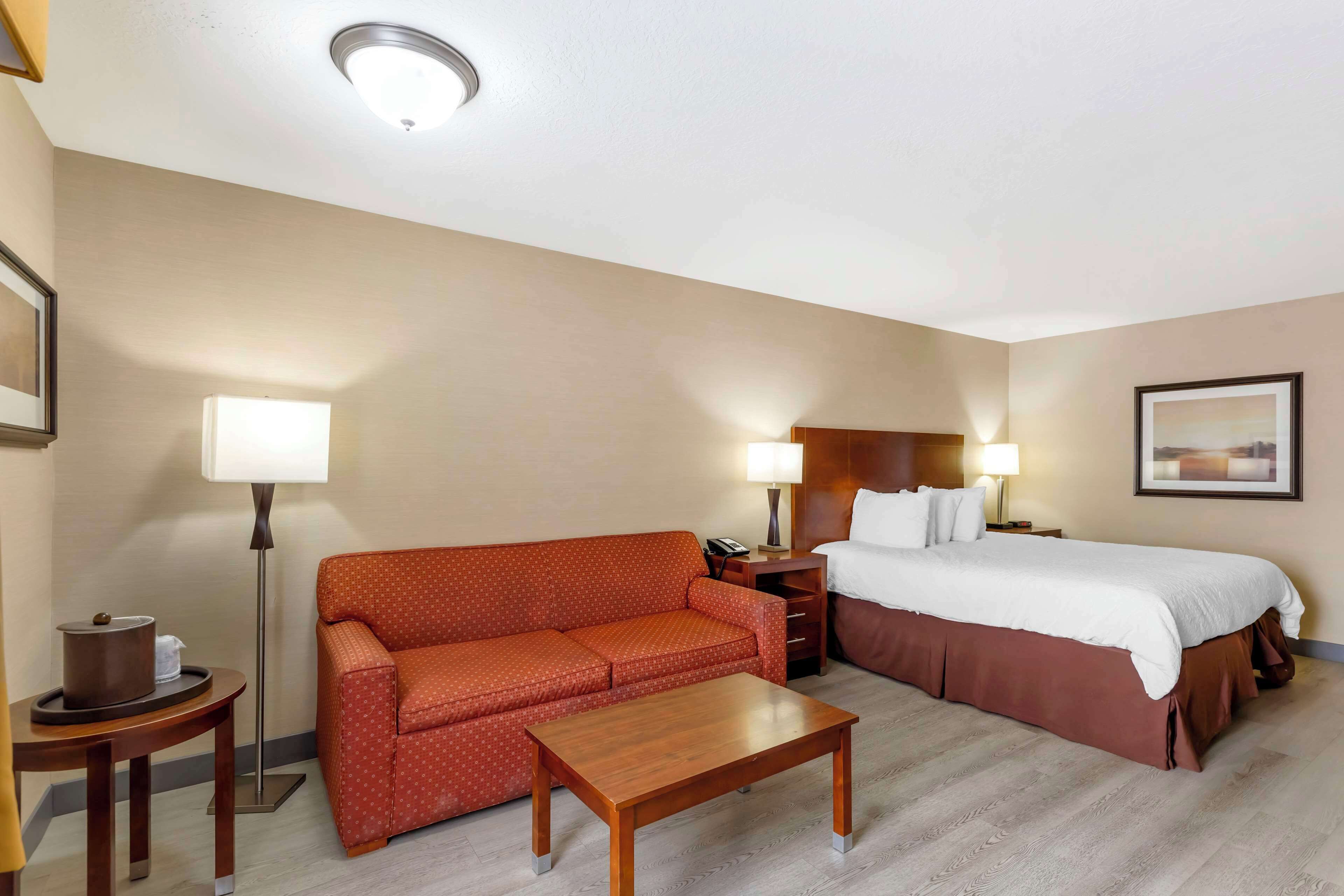 A hotel room with a bed, a sofa, a coffee table, a nightstand, and a lamp.