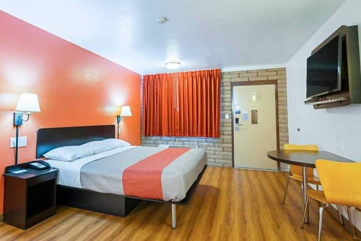 A hotel room with a bed, bedside lamps, a TV, a small table with chairs, and a door.